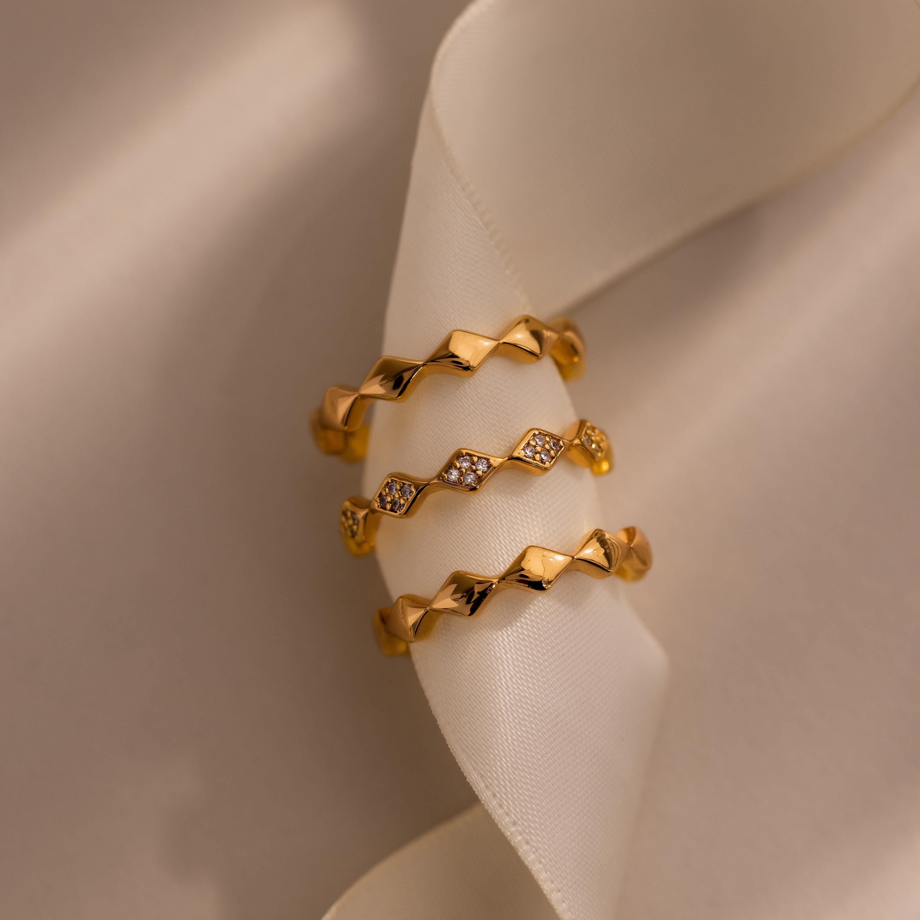 Set of three eternity curve rings in gold, featuring quilted wave design with one band accented by sparkling diamonds, displayed on soft ivory fabric.