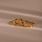 Set of three gold eternity curve rings with quilted wave design, including one with diamond accents, displayed on a soft neutral surface.