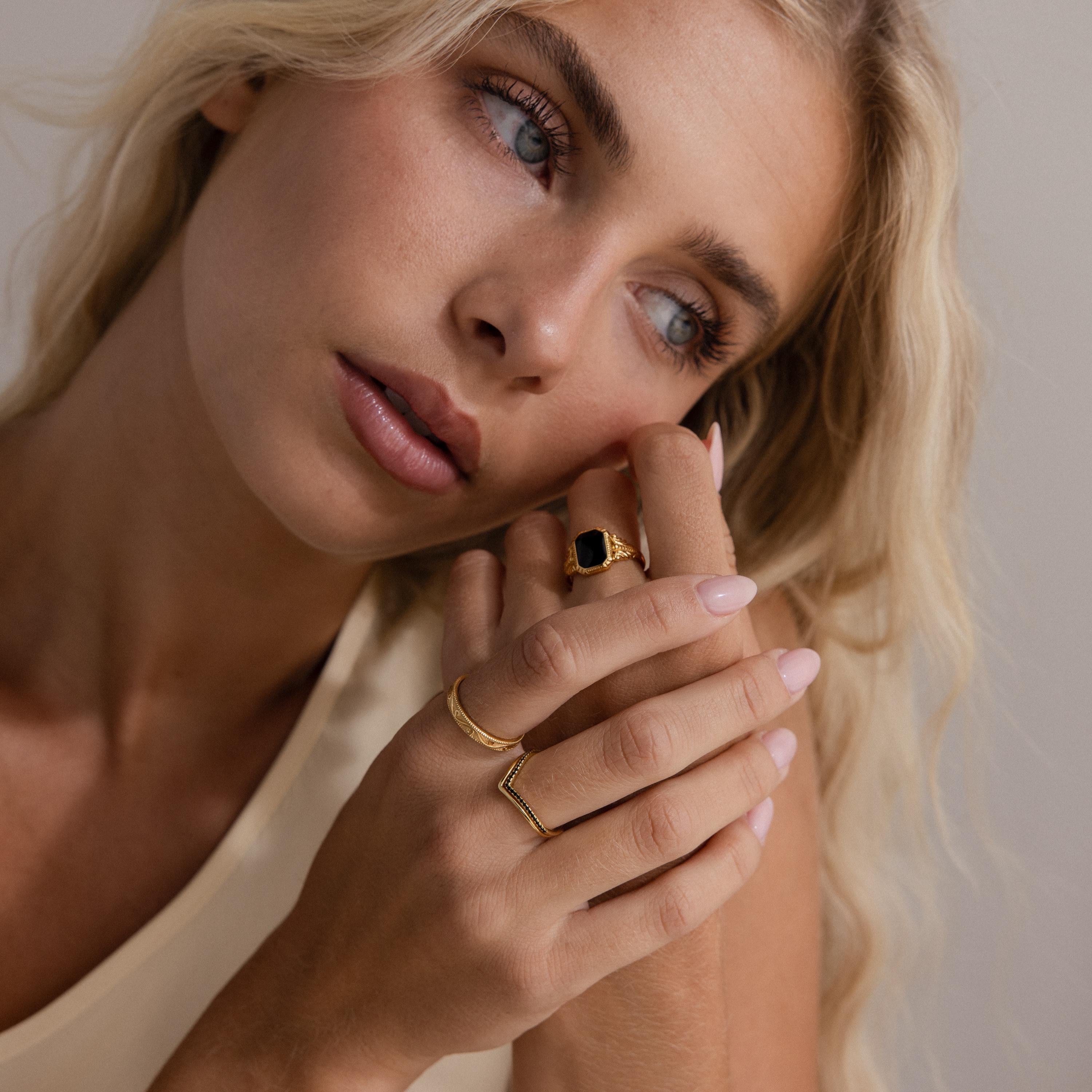 Woman wearing multiple gold rings, including a bold black stone ring and a chevron stacking ring with black stones.