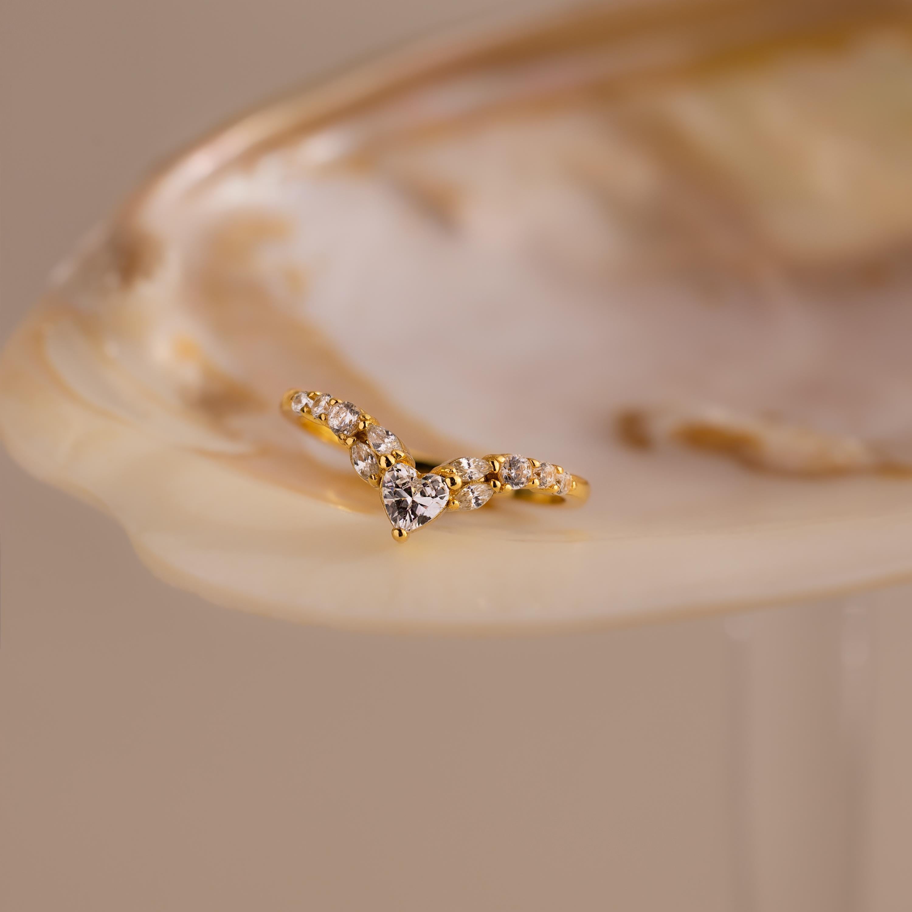 Gold heart curve cluster diamond ring with a heart shaped center stone and round diamonds displayed on a seashell.