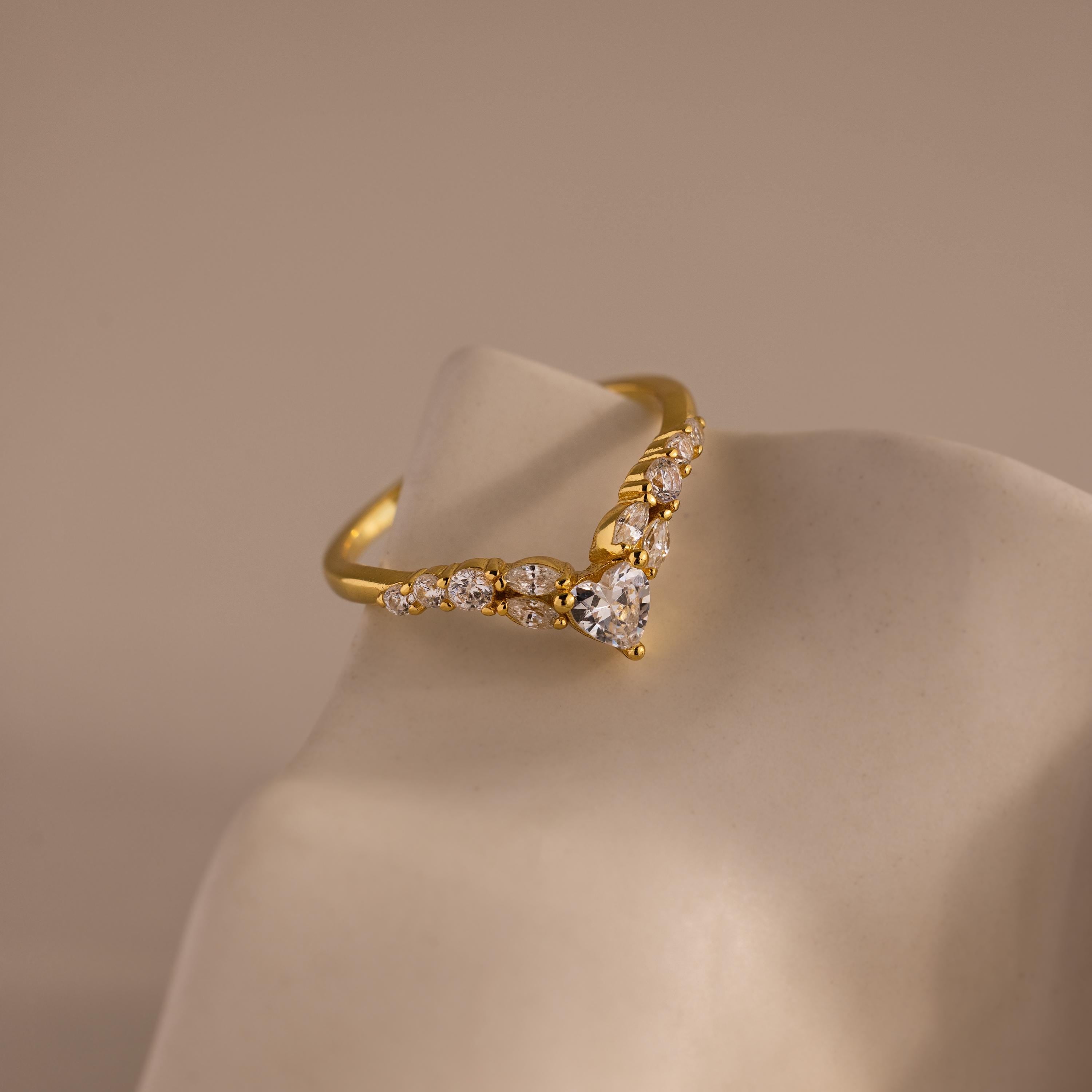 Gold heart curve cluster diamond ring featuring a central heart shaped stone with a row of round and marquise diamonds set in a V shaped band.