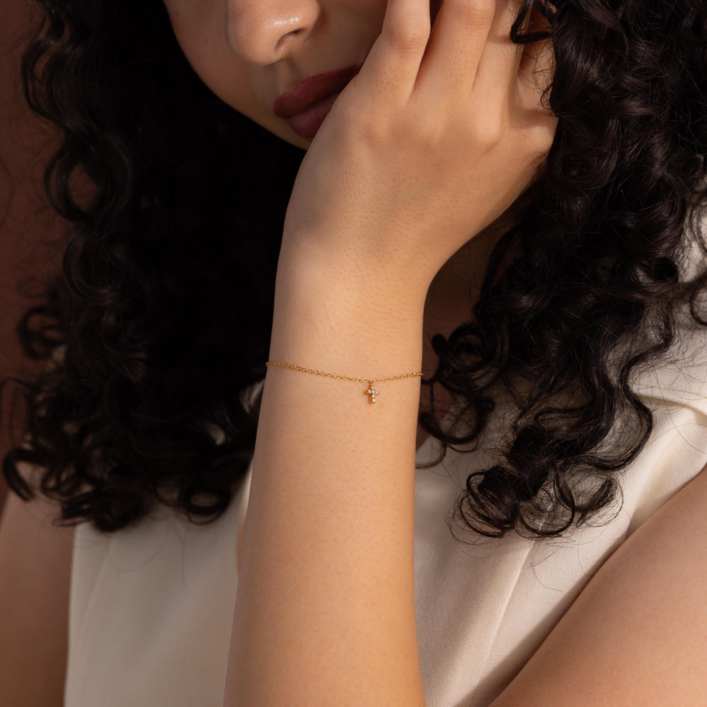 Gold chain bracelet with a dainty crystal cross charm, worn on the wrist for a minimalist and elegant jewelry look that blends faith inspired design with timeless everyday style.