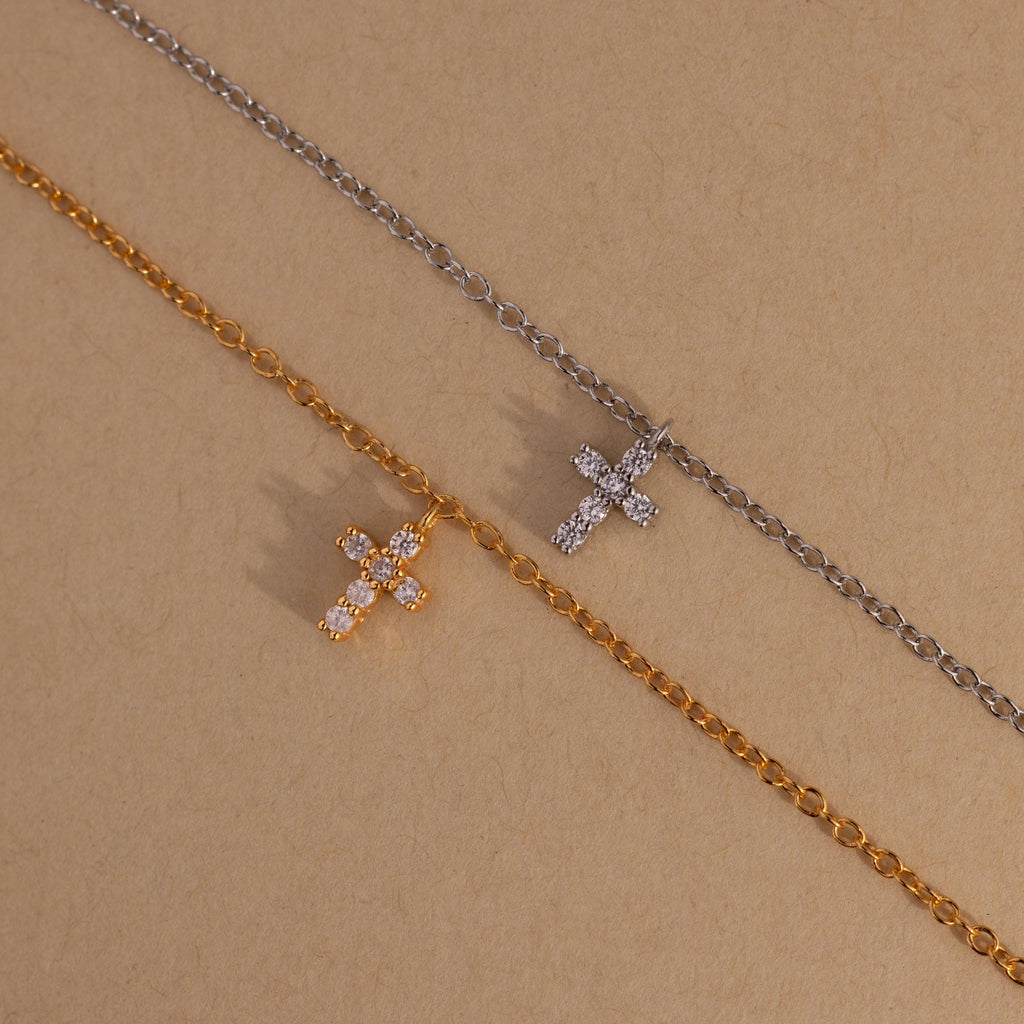 Gold and silver chain necklaces with small jeweled cross pendants pair beautifully with a dainty bracelet or the Dainty Cross Charm Bracelet, displayed on a plain beige background.