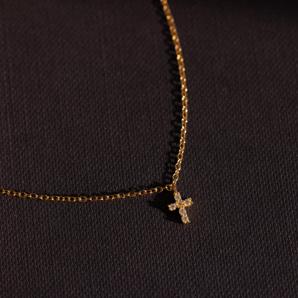 Gold chain bracelet featuring a sparkling crystal cross charm, photographed against a dark textured background for a bold and elegant presentation.