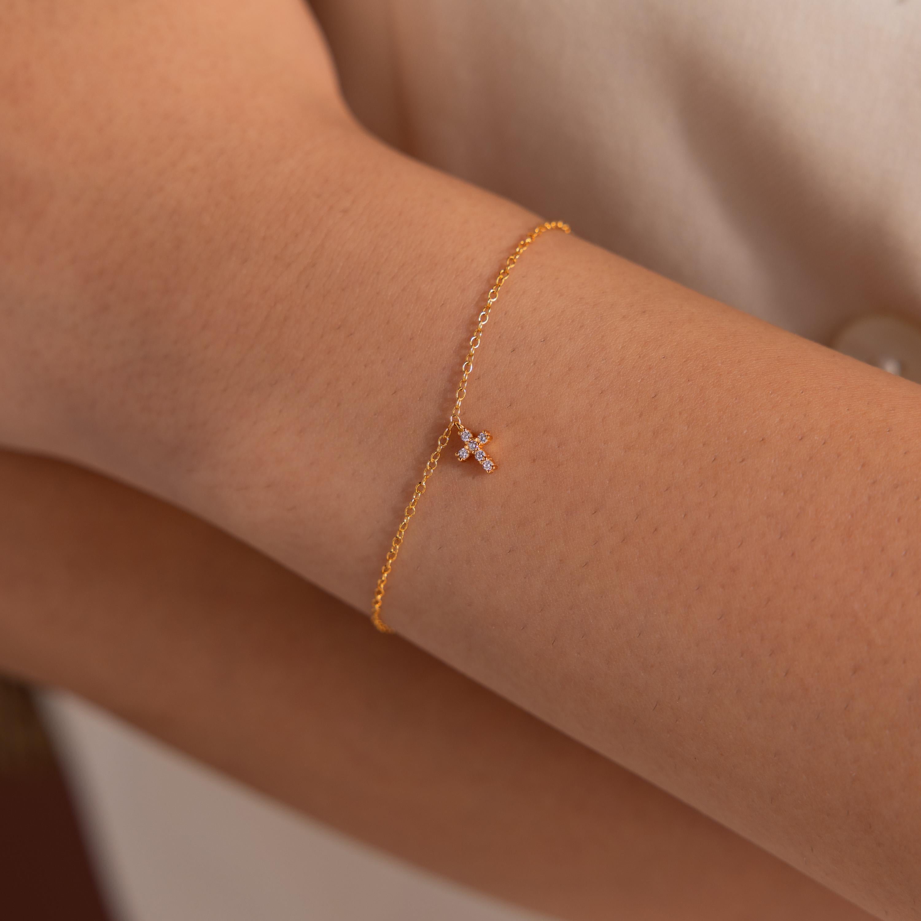 Delicate gold chain bracelet featuring a tiny cross charm adorned with sparkling diamonds, minimalist and elegant jewelry piece.