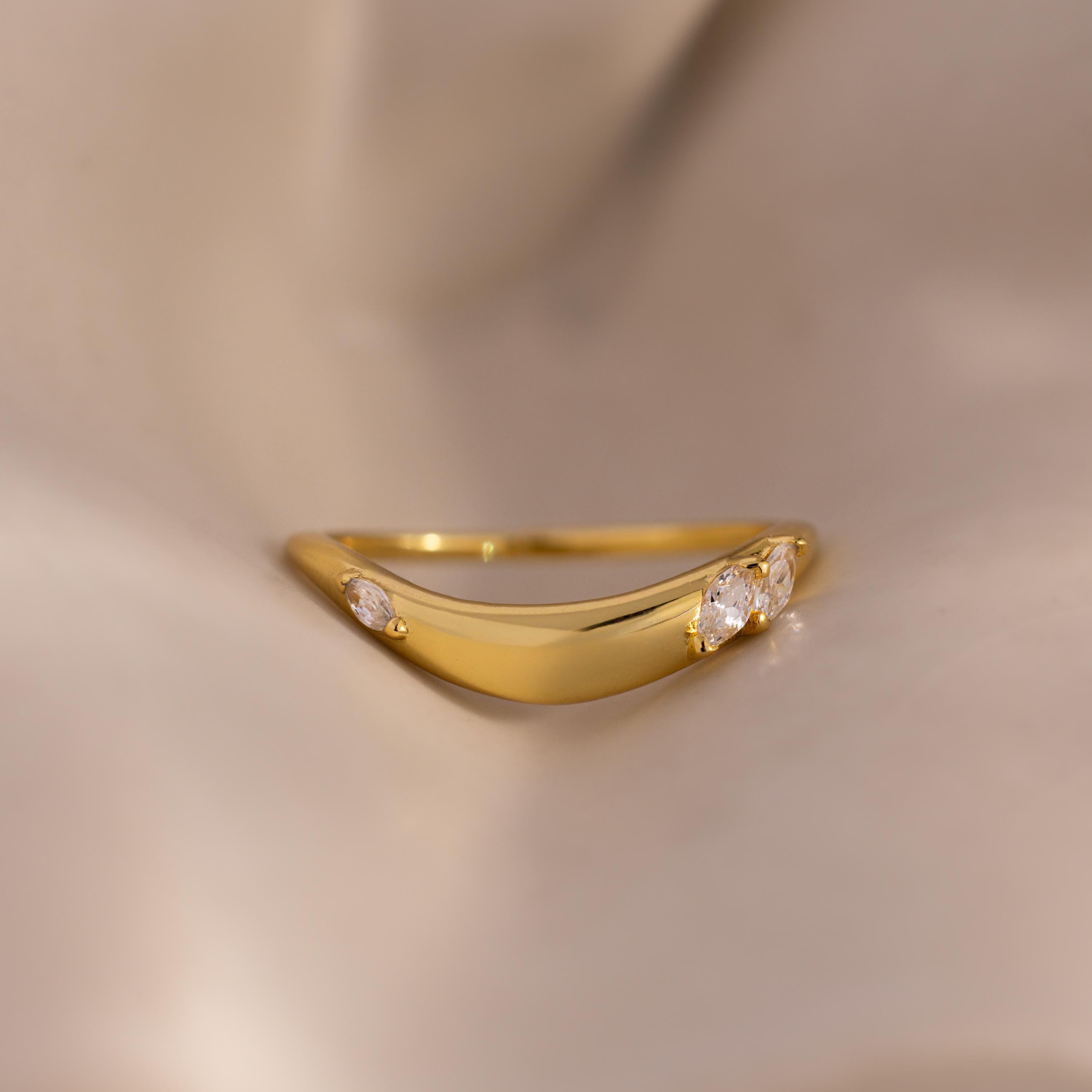 Close up of a gold curved band ring with three marquise-cut white gemstones, displayed on soft beige fabric for a minimal and elegant jewelry presentation.
