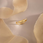 Gold curved band ring with three marquise cut clear gemstones, displayed on soft beige fabric for an elegant and minimal jewelry presentation.