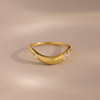 Gold curved band ring with three marquise cut clear gemstones set along the front, displayed on a neutral beige background.