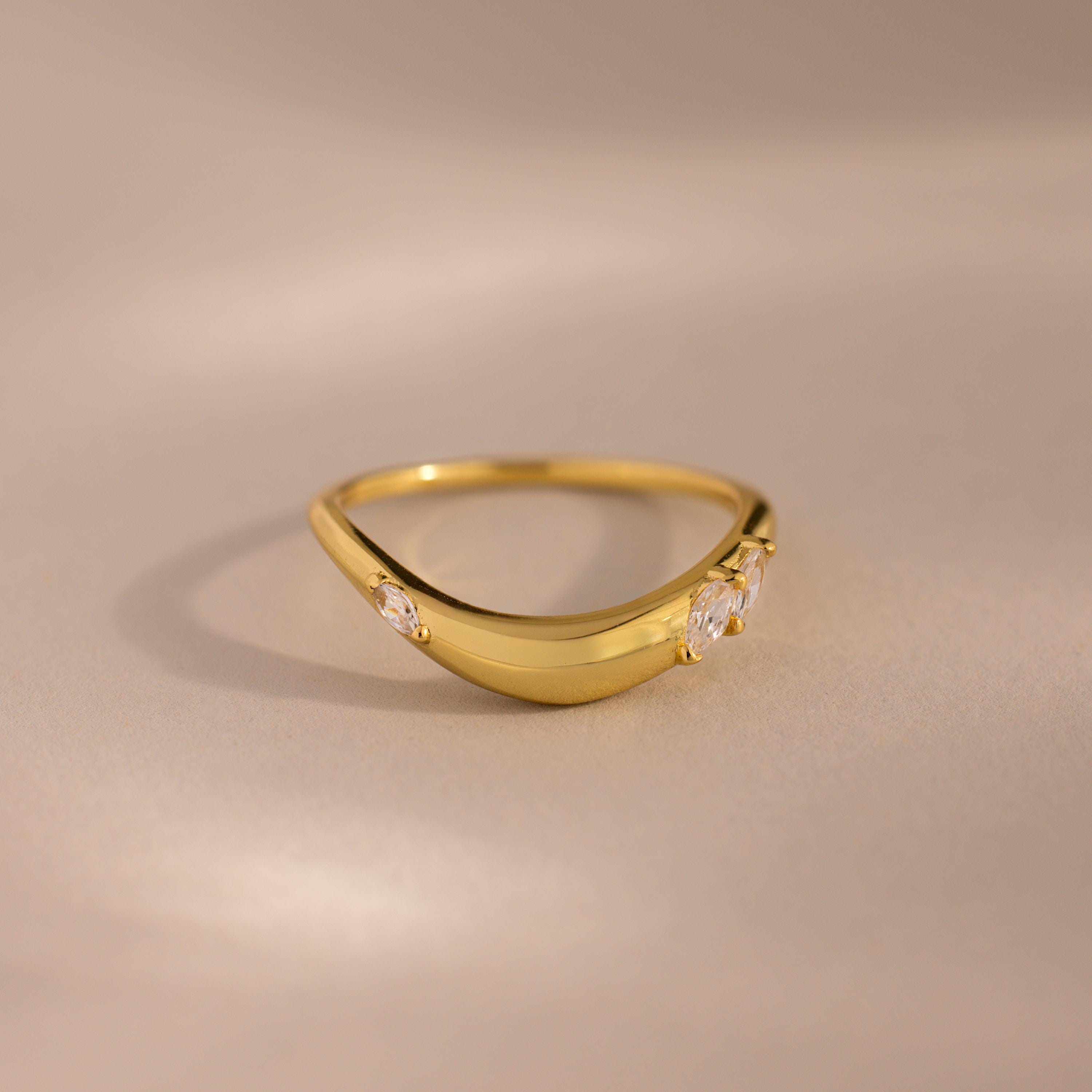 Gold curved band ring with three marquise cut clear gemstones set along the front, displayed on a neutral beige background.