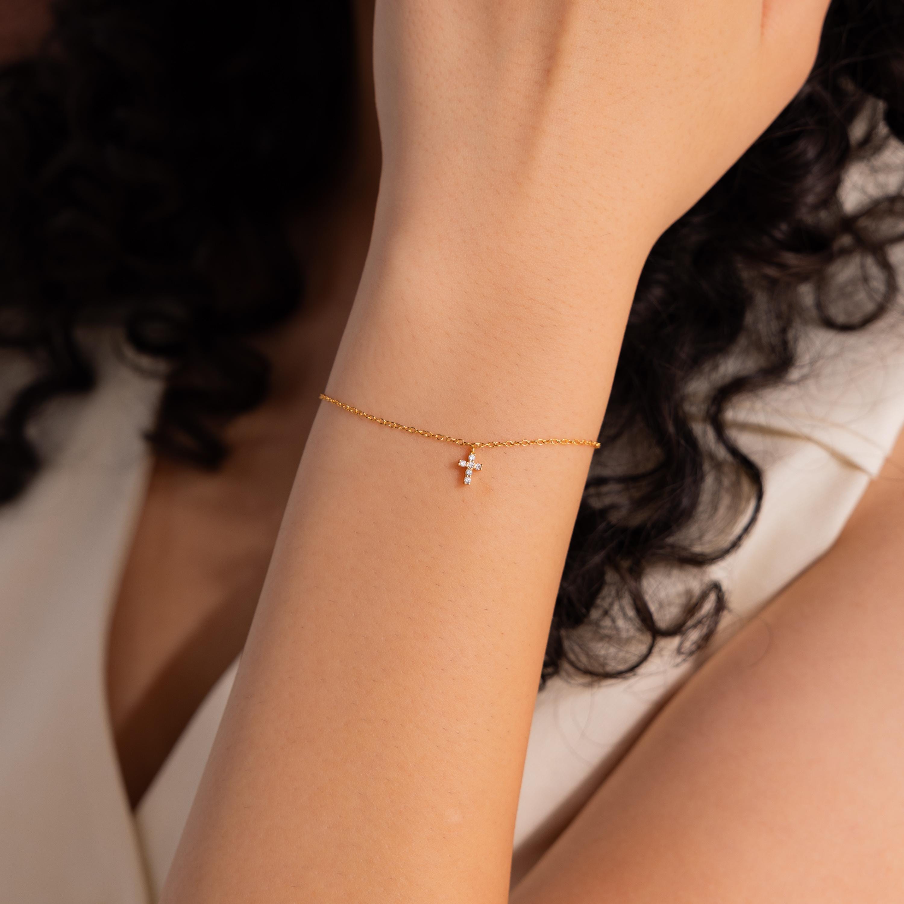 Gold chain bracelet with a delicate crystal cross charm, styled on the wrist for an elegant and minimal look, perfect for layering or everyday wear.