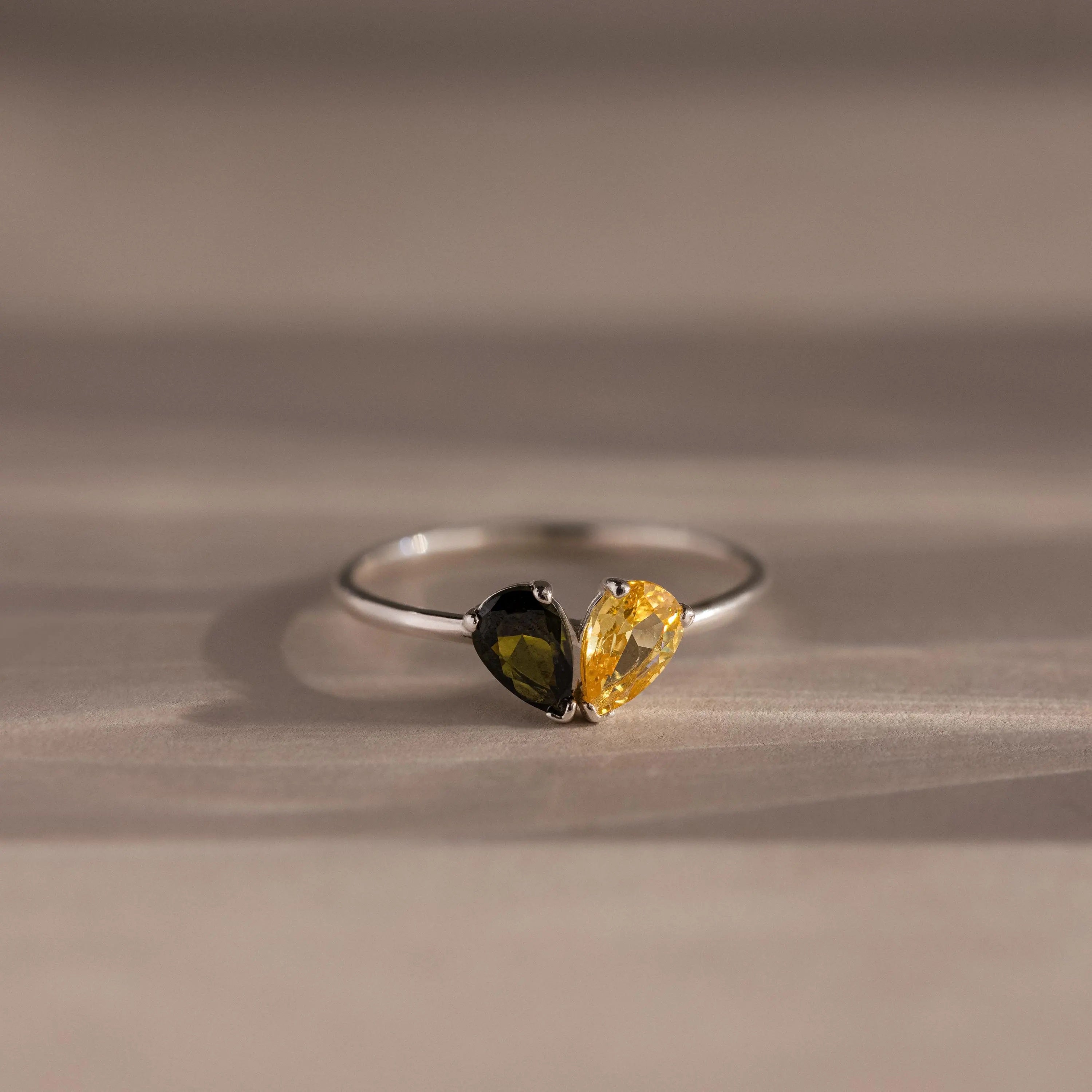 The Toi et Moi Teardrop Heart Ring in Sterling Silver features two pear-cut stones—one black and one yellow—set side by side on a polished silver band.