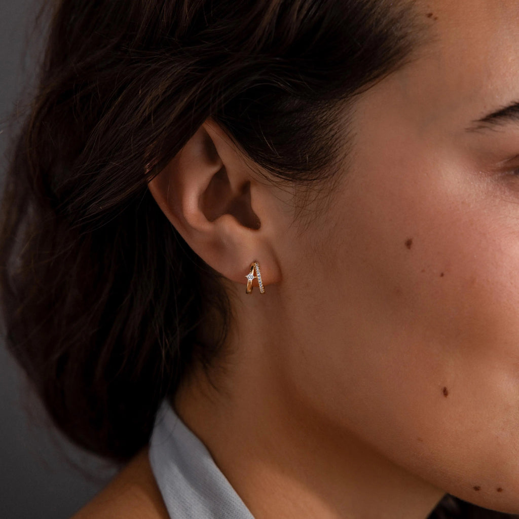 Close-up of a woman's ear wearing elegant earrings—a small gold letter A stud—paired with Pave Diamond Duo Huggies, her hair tucked behind her ear.