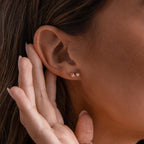 A woman's ear is adorned with Marquise Onyx & Pearl Studs, featuring a striking gold design; her hand is gently poised near her elegant earrings.
