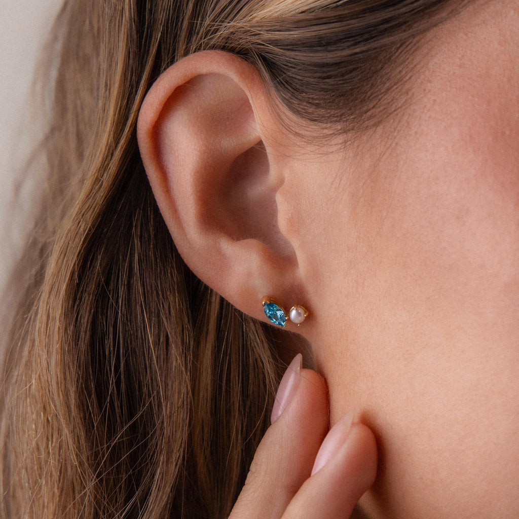 Close-up of a woman's ear wearing Marquise Topaz & Pearl Studs, elegant toi et moi earrings featuring a blue marquise topaz paired with a delicate pearl.
