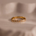 The Diamond Cluster Eternity Ring, featuring sparkling diamonds encircling the band, is displayed on a soft, cream-colored surface.