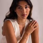 Woman wearing layered gold and pearl necklaces with matching gold and pearl bracelet, styled with a cream knit top for an elegant, modern look.