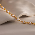 Close up of a gold pearl chain necklace with small white pearls set in oval gold links, displayed on a soft neutral fabric background.
