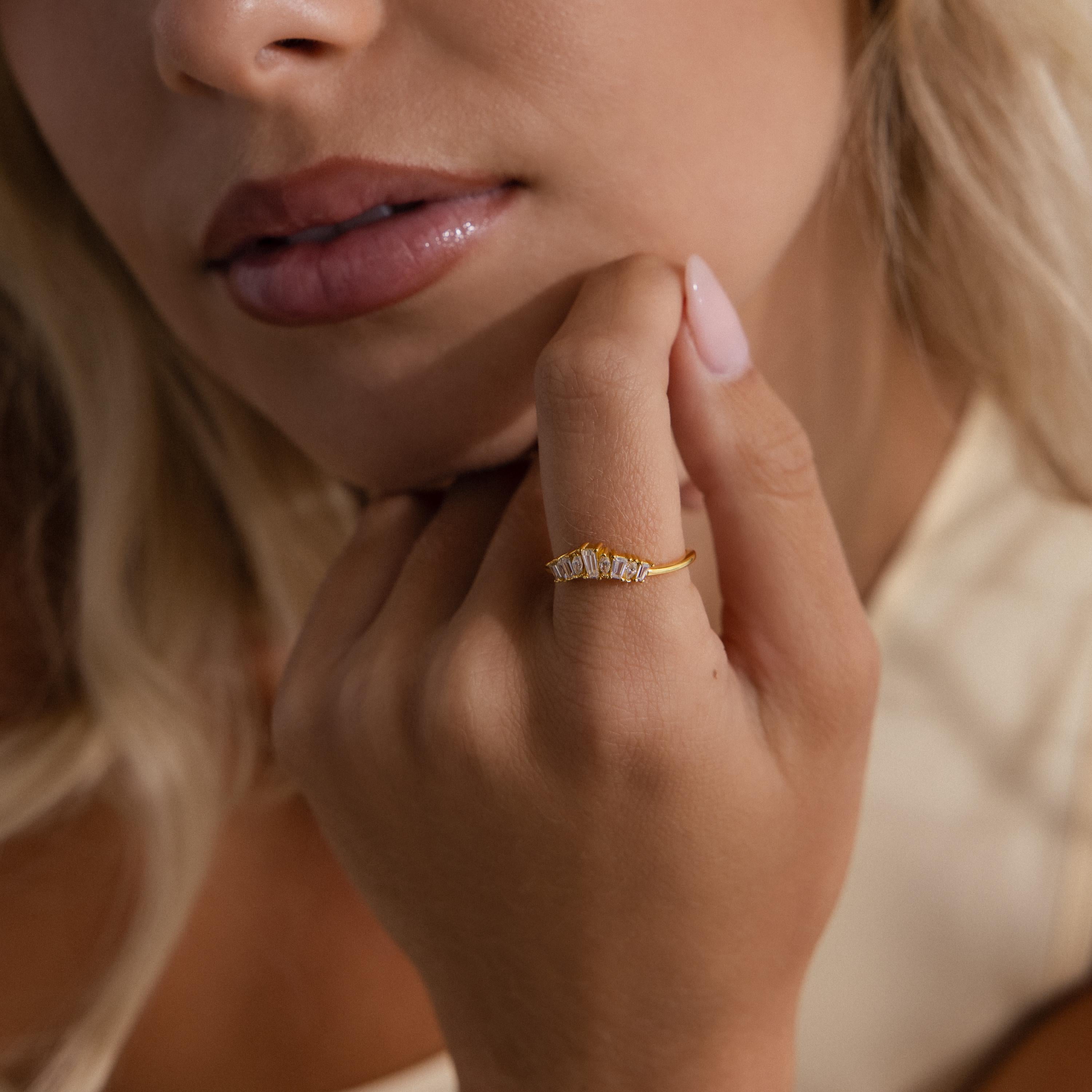 Woman wearing a slim gold ring with a row of tapered baguette and marquise cut clear stones, shown close up on her hand near her face for an elegant and refined look.