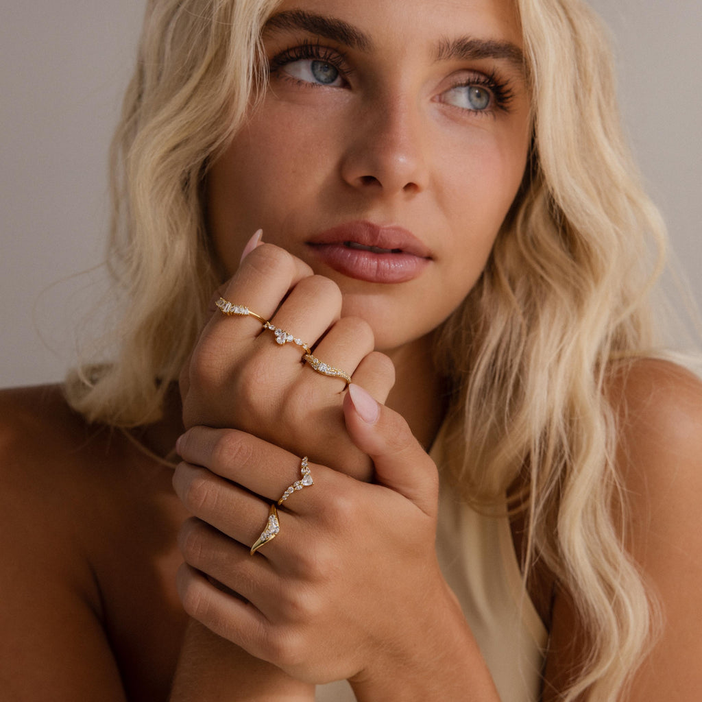 Woman wearing multiple delicate gold rings with clear baguette and marquise cut stones, styled on both hands for a layered, elegant, and modern look.
