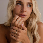 Woman wearing multiple delicate gold rings with clear baguette and marquise cut stones, styled on both hands for a layered, elegant, and modern look.