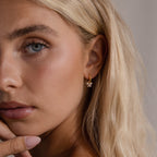 Woman wearing the Starlight Bow Hoop earring in gold, featuring a small hoop with sparkling baguette-cut stones in a bow shaped design, styled for an elegant and modern look.