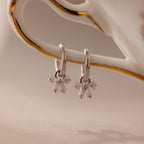 Silver Starlight Bow Hoop earrings with dangling baguette cut clear stones in a bow shaped design, displayed hanging from a porcelain handle with gold detail.