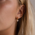 Close up of a woman wearing the Starlight Bow Hoop earrings in silver, featuring a sleek hoop with dangling baguette cut clear stones arranged in a sparkling bow design.