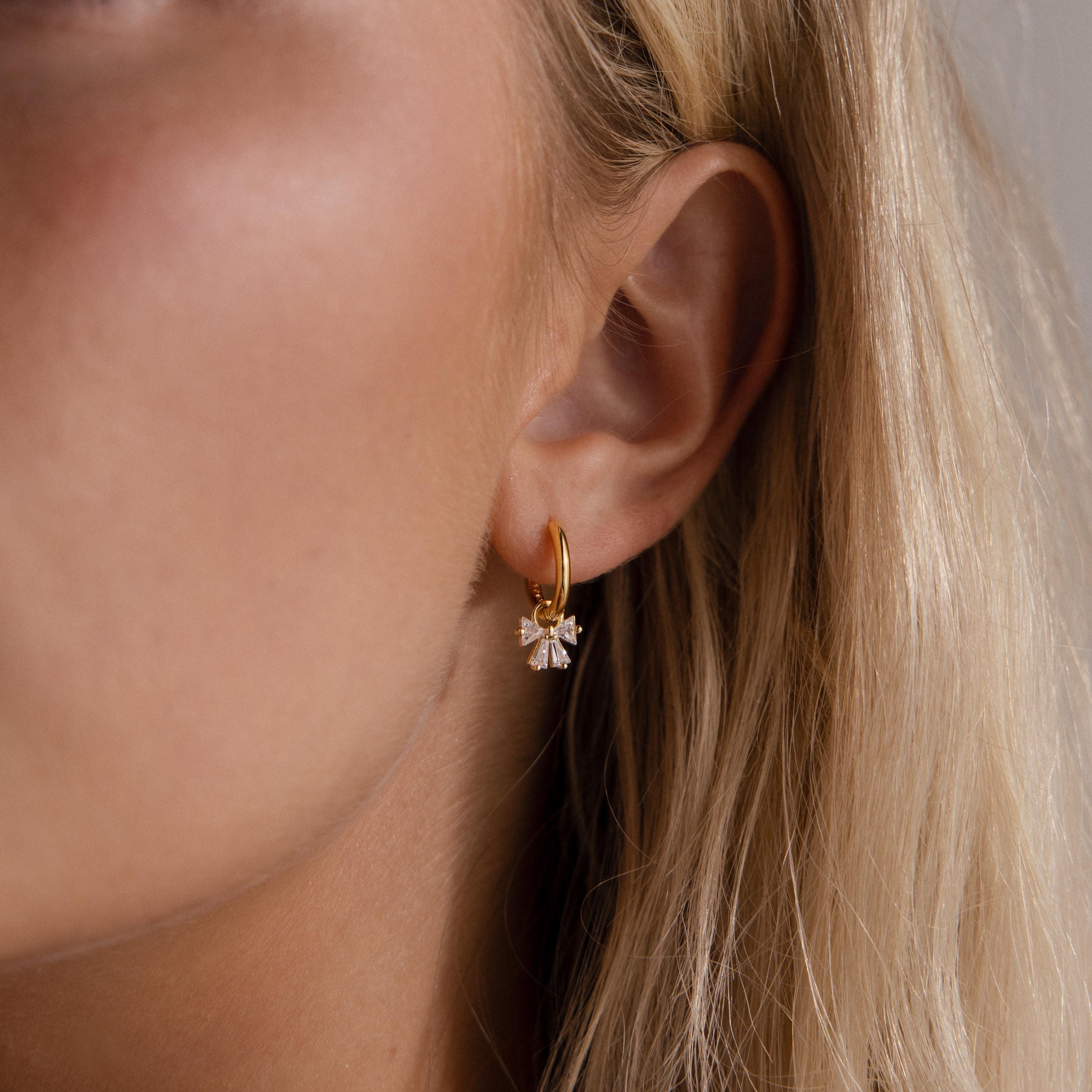 Close up of a woman wearing the Starlight Bow Hoop earrings in silver, featuring a sleek hoop with dangling baguette cut clear stones arranged in a sparkling bow design.