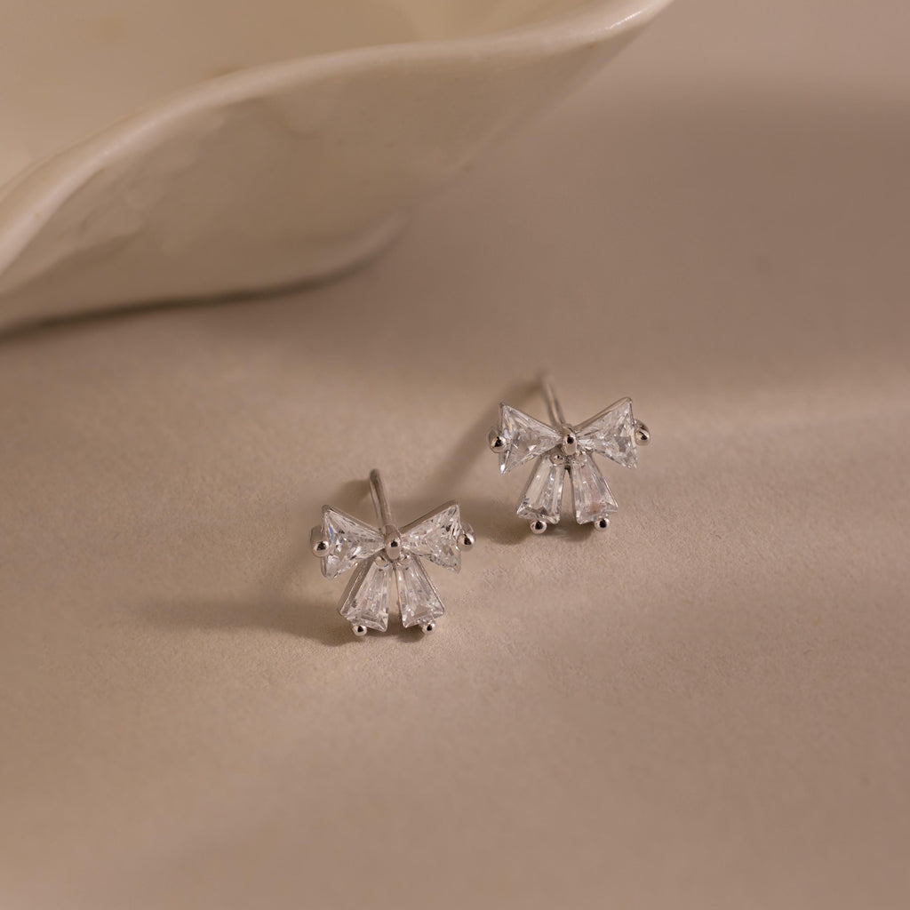 Silver Starlight Bow stud earrings with baguette-cut clear stones arranged in a delicate bow design, displayed on a soft neutral background for an elegant presentation.