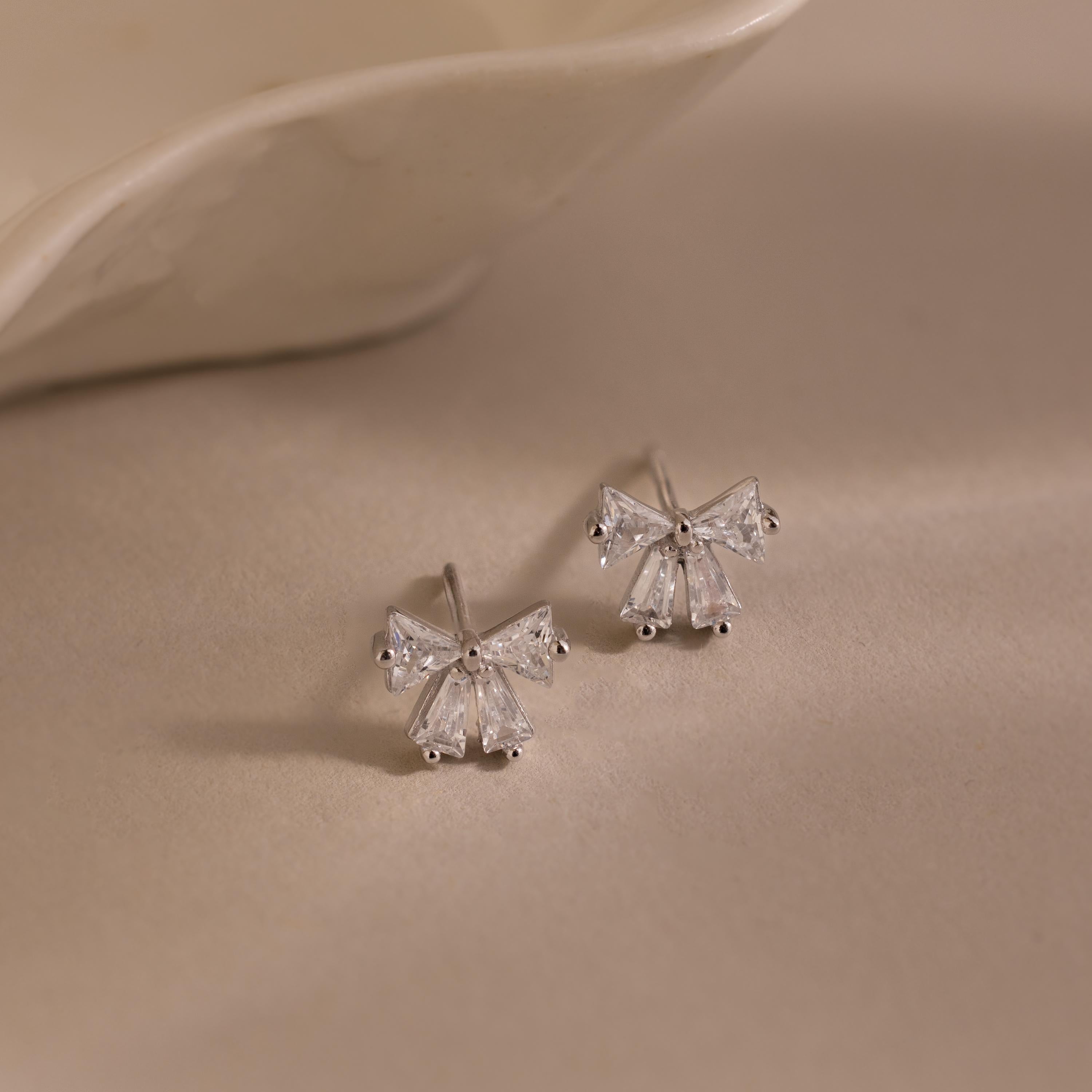 Silver Starlight Bow stud earrings with baguette-cut clear stones arranged in a delicate bow design, displayed on a soft neutral background for an elegant presentation.