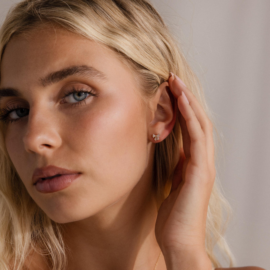 Woman wearing the Starlight Bow stud earring in gold, featuring baguette-cut clear stones in a delicate bow design, styled for a subtle and elegant everyday look.