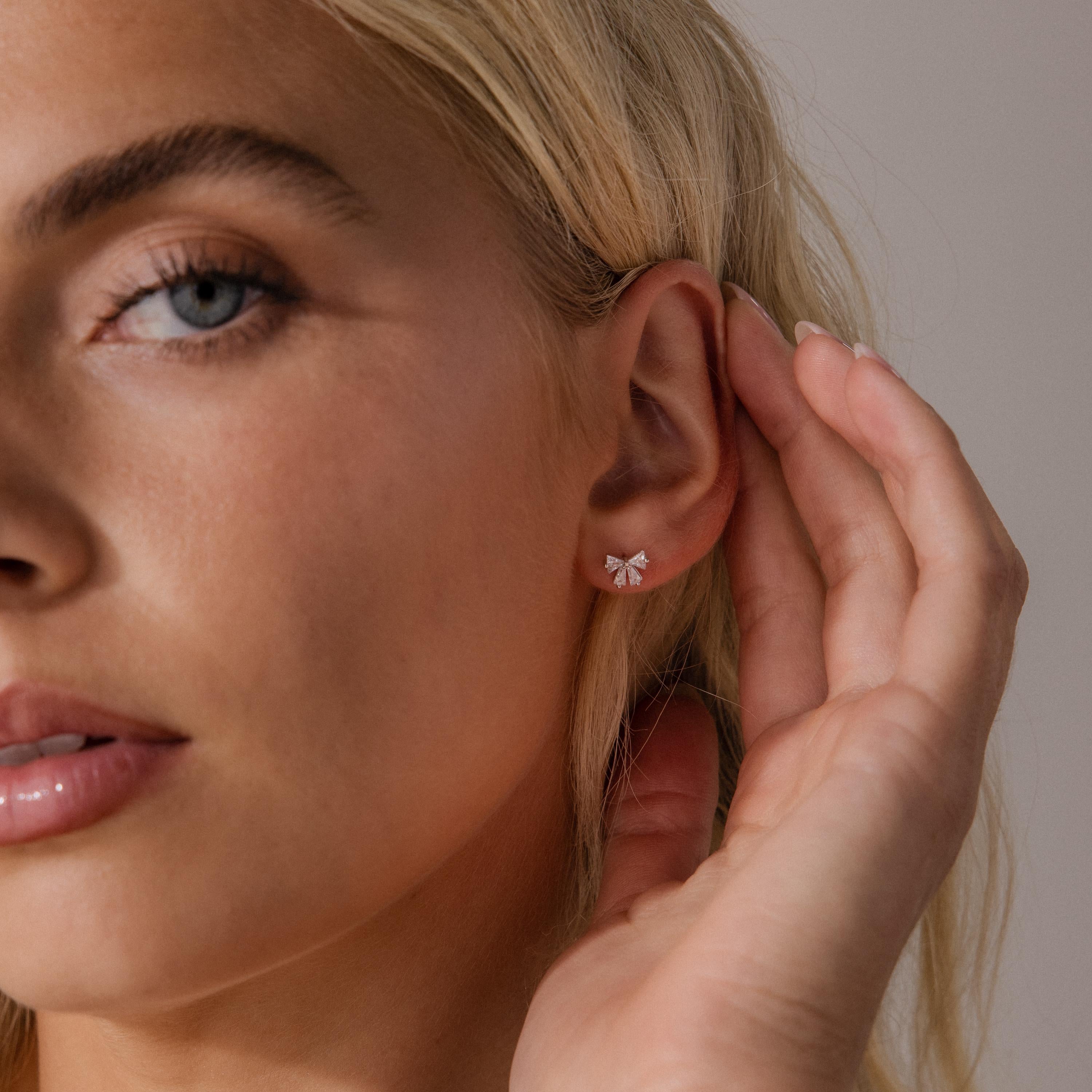 Close up of a woman wearing the Starlight Bow stud earring in silver, featuring baguette cut clear stones in a delicate bow design for a subtle and elegant look.