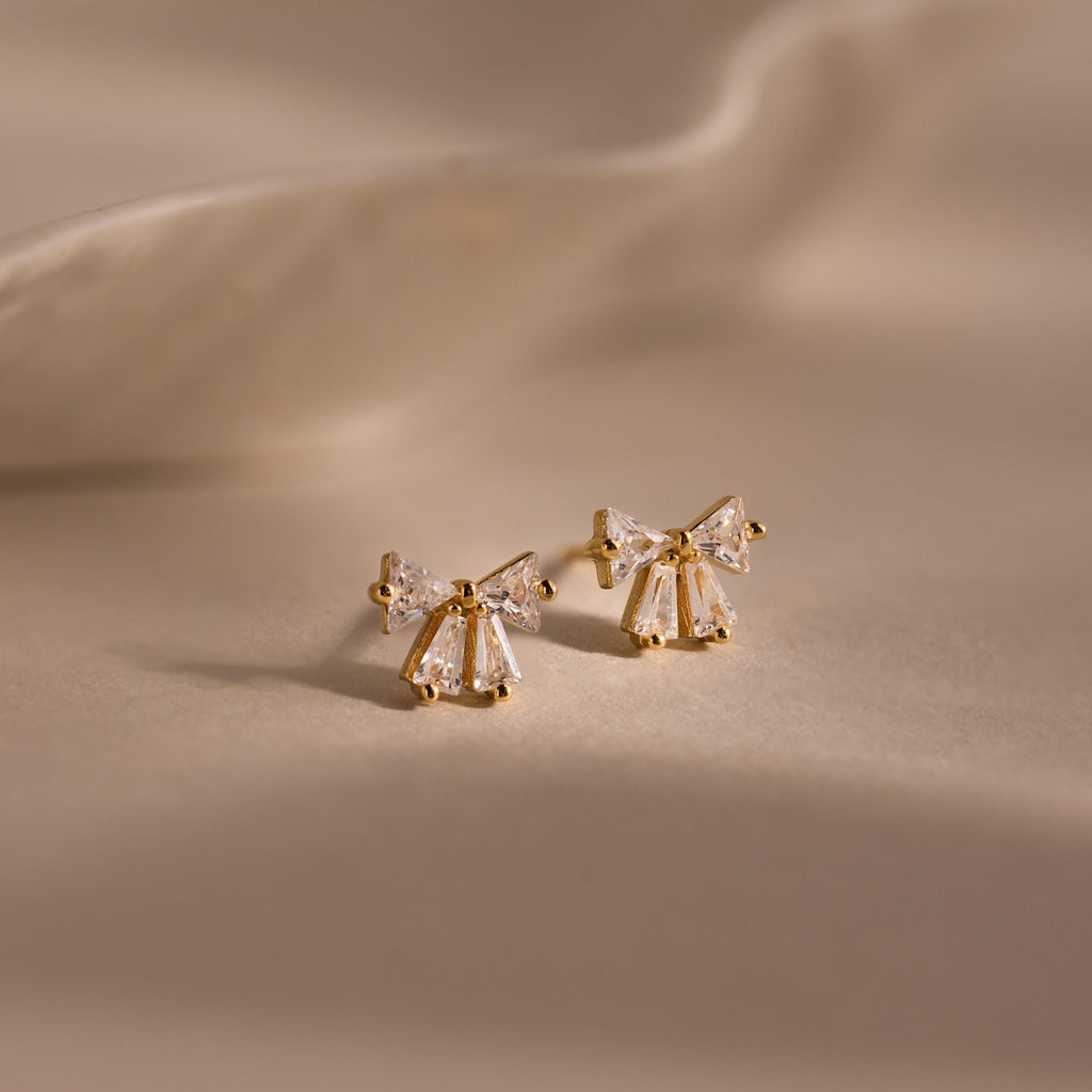 Gold Starlight Bow stud earrings with baguette cut clear stones arranged in a delicate bow design, displayed on a soft neutral background for an elegant look.