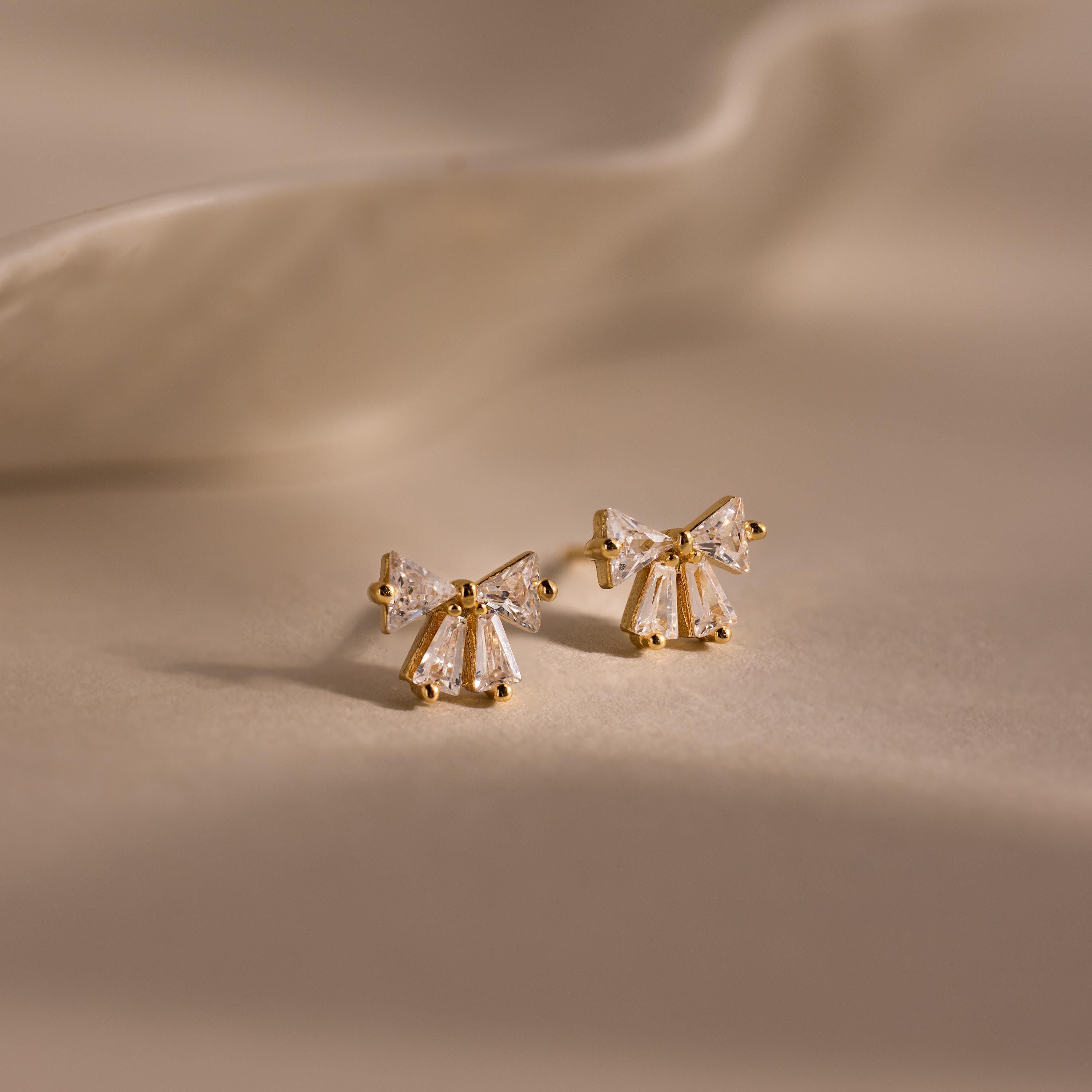 Gold Starlight Bow stud earrings with baguette cut clear stones arranged in a delicate bow design, displayed on a soft neutral background for an elegant look.