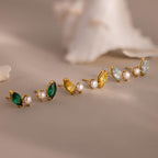 The Marquise Birthstone & Pearl Studs set features three pairs of gold stud earrings with marquise birthstones in green, yellow, and blue accents, plus classic pearl studs, elegantly arranged on a beige surface.