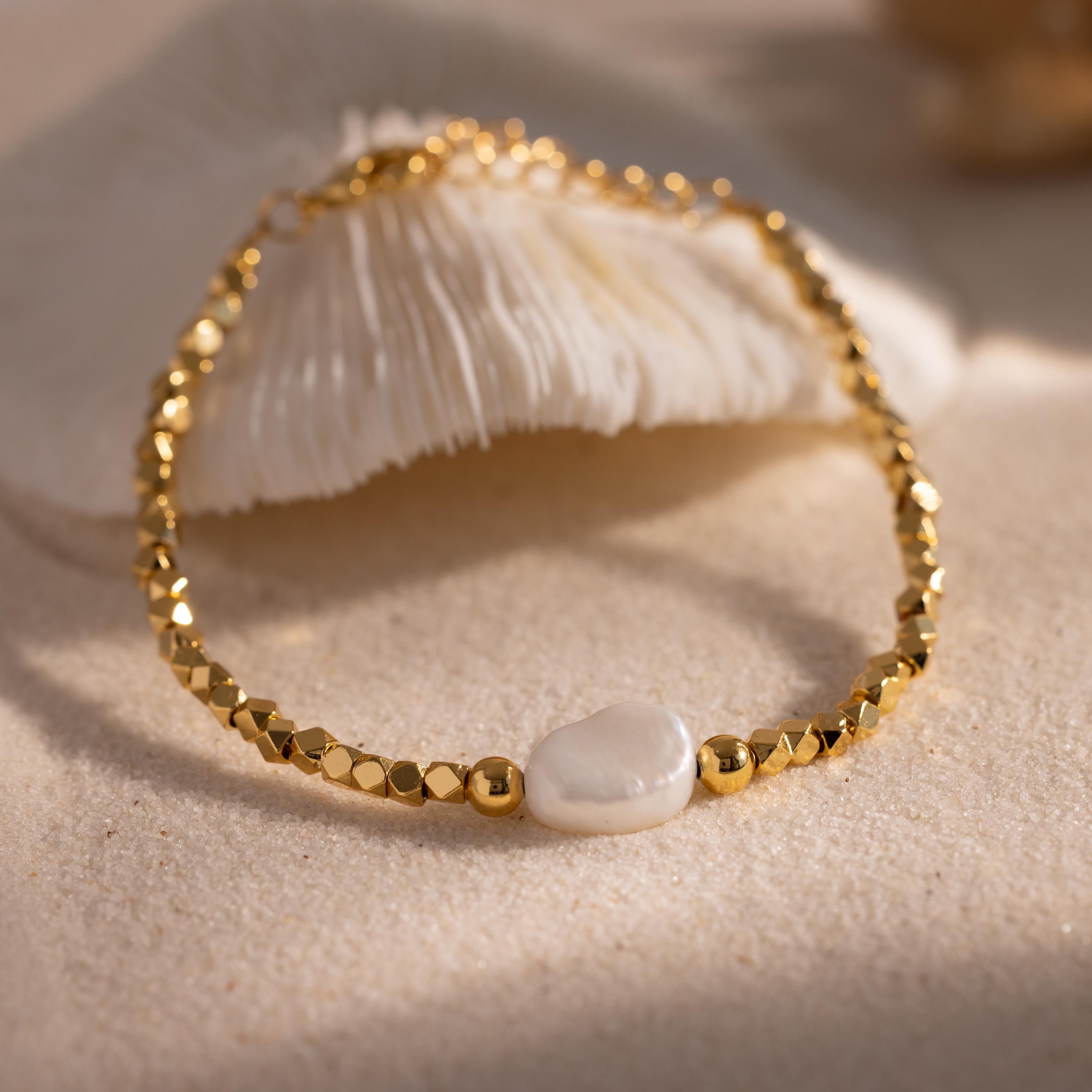 Beaded Pearl Bracelet crafted with faceted gold beads and accented by a single natural white pearl centerpiece, displayed on a sandy surface for a refined, coastal inspired look.