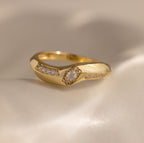 Close up of the Radiant Facet Ring in polished gold featuring a diamond shaped CZ stone in center with pave set side stones, displayed on a smooth ivory surface.
