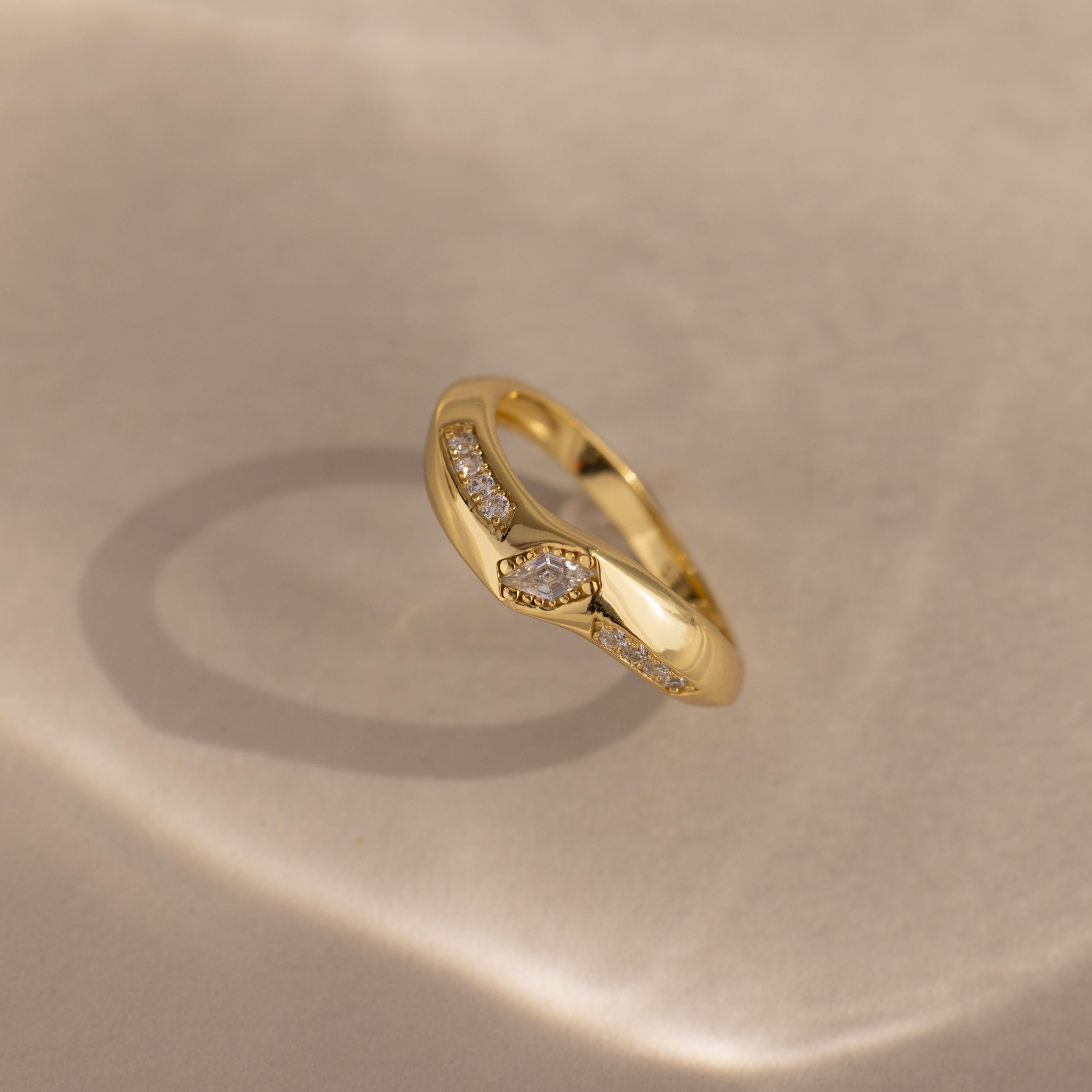 Radiant Facet Ring in polished gold featuring diamond shaped CZ stones with pave set side stones, displayed on a softly lit neutral surface with shadow detail.