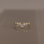 Radiant Tear Ring in polished gold featuring a pear cut diamond center accented by round and marquise diamonds, displayed on a reflective neutral surface.
