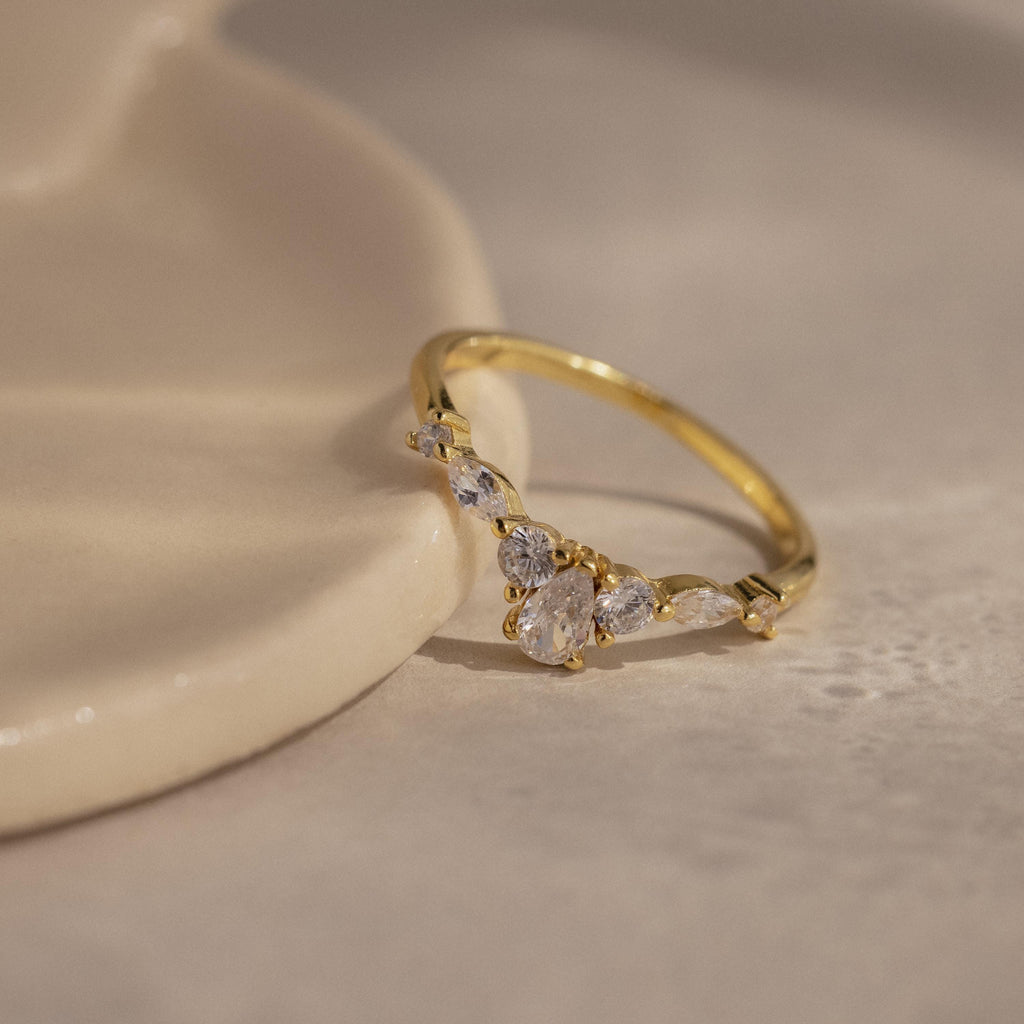 Radiant Tear Ring in polished gold featuring a pear cut diamond center with round and marquise side stones, displayed on a smooth neutral surface.