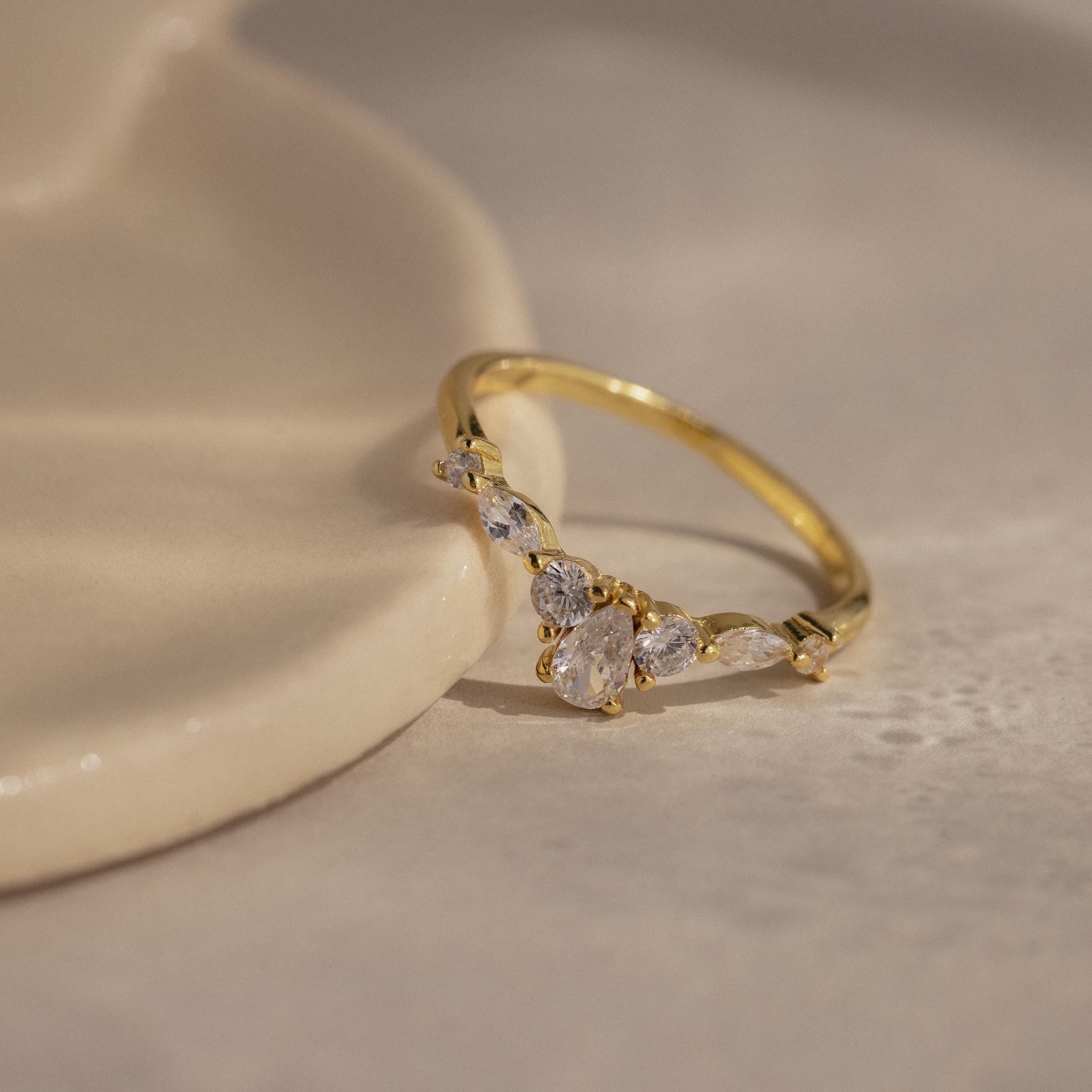Radiant Tear Ring in polished gold featuring a pear cut diamond center with round and marquise side stones, displayed on a smooth neutral surface.