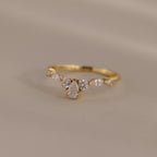 Radiant Tear Ring in polished gold with a pear cut diamond center framed by round and marquise side stones, displayed on a soft neutral background.