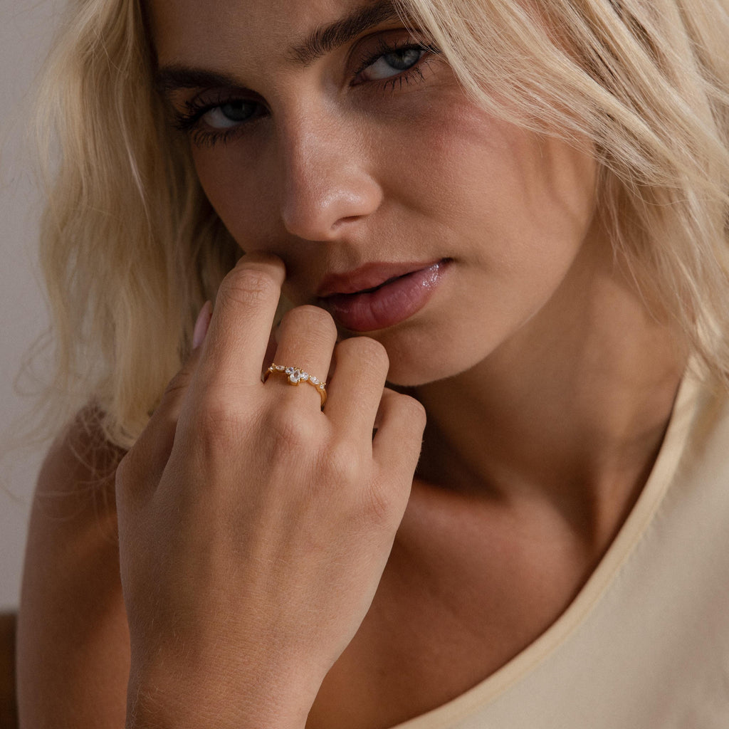 Woman wearing the Radiant Tear Ring in gold with a pear cut diamond center and marquise side stones, styled with glossy lips and a neutral one shoulder top.