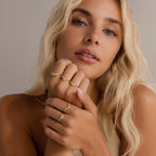 Woman wearing stacked gold rings including the Radiant Tear Ring and Radiant Facet Ring, both with diamond detailing, styled with loose blonde waves and natural makeup.