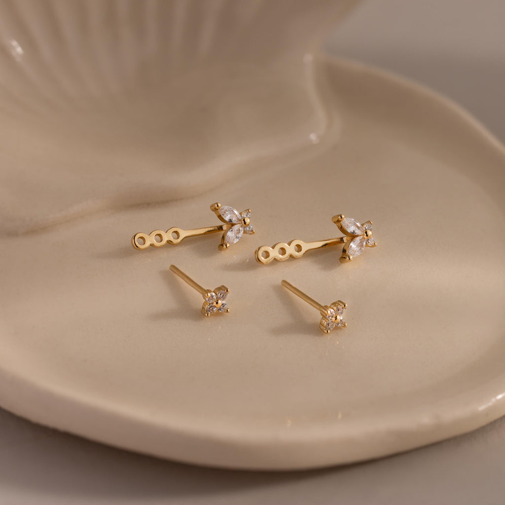 Gold stud earrings with diamond clusters and detachable butterfly shaped drops, displayed on a glossy ceramic dish.