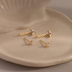 Gold stud earrings with diamond clusters and detachable butterfly shaped drops, displayed on a glossy ceramic dish.