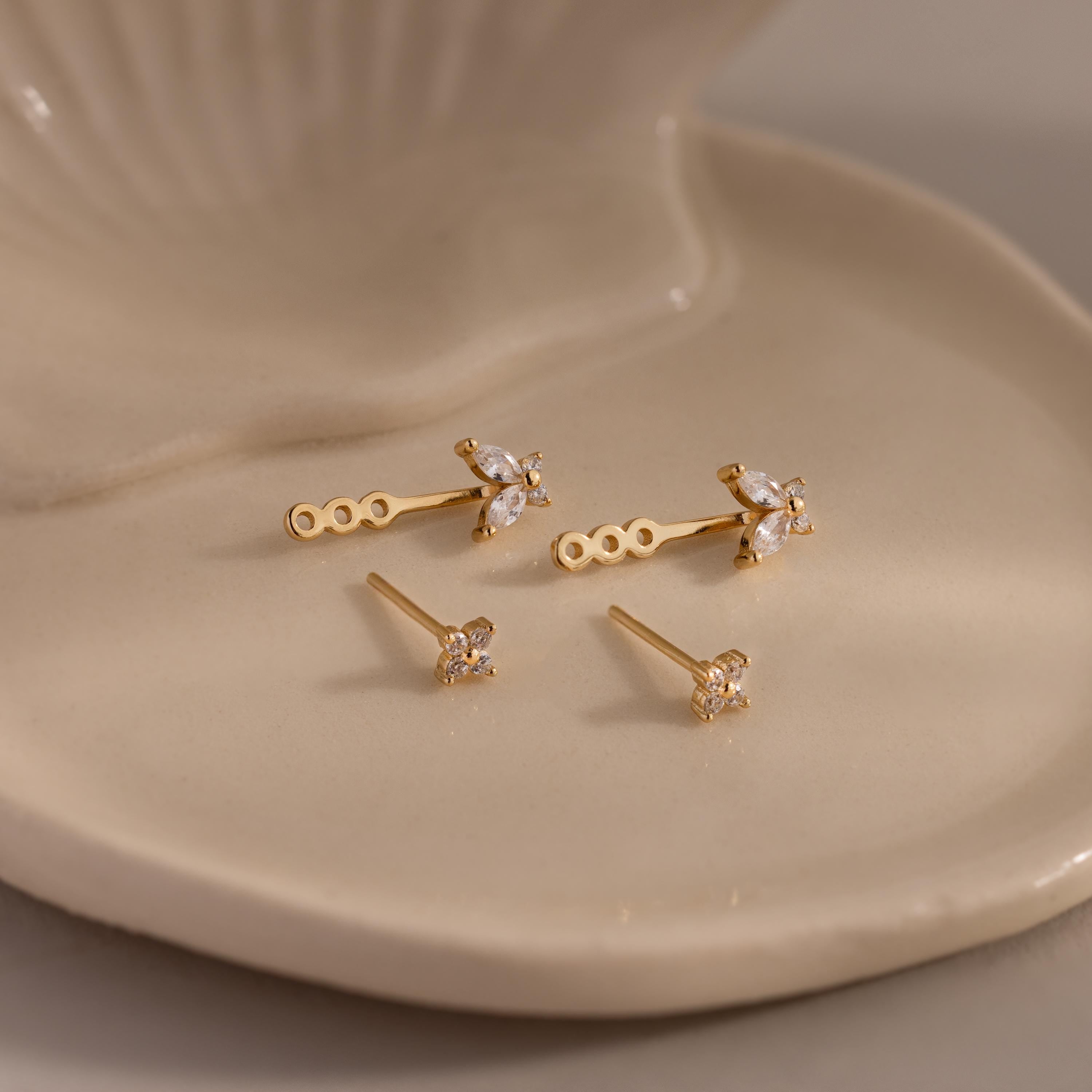 Gold stud earrings with diamond clusters and detachable butterfly shaped drops, displayed on a glossy ceramic dish.