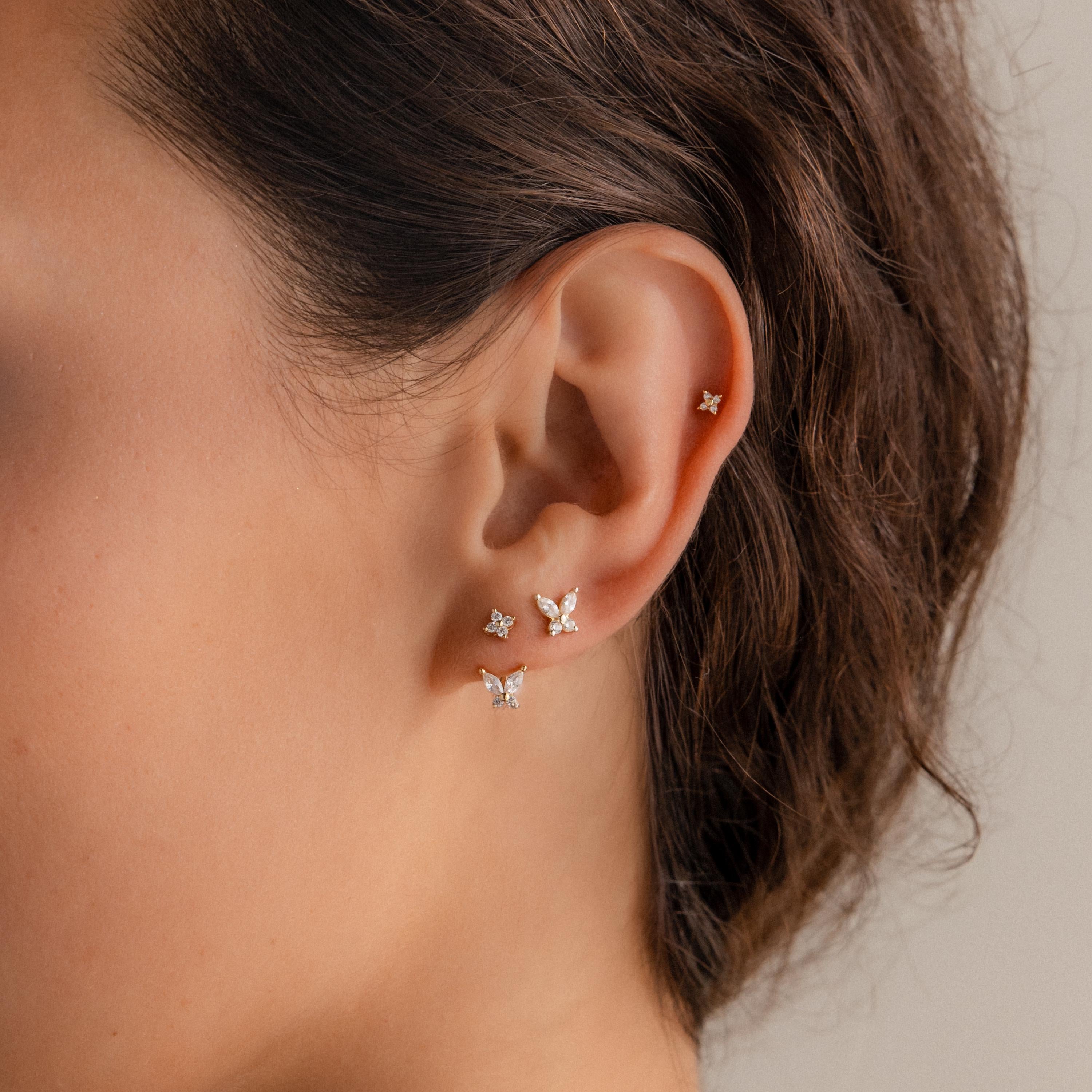 Woman wearing multiple gold stud earrings with diamond clusters and butterfly shaped drops, styled in a curated ear stack look.