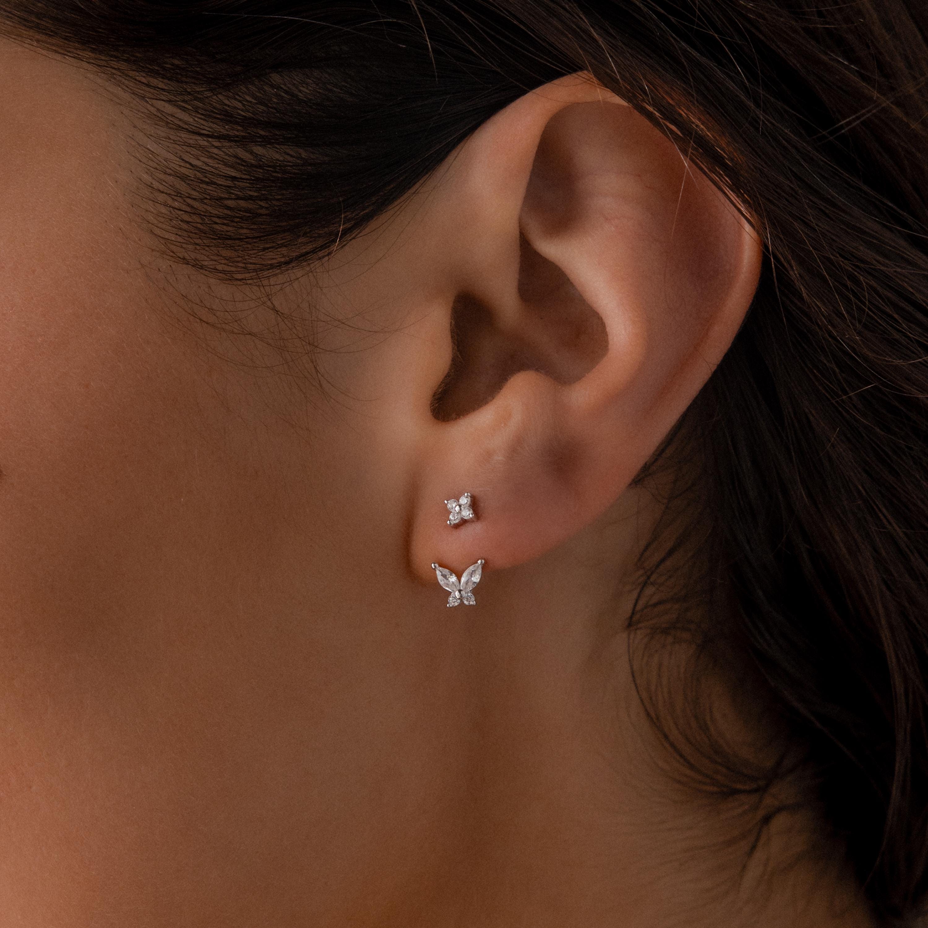 Silver stud earrings with diamond clusters paired with detachable butterfly shaped drops, worn on the ear for a delicate layered look.