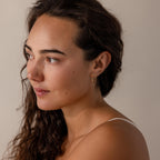 Woman with wavy brown hair wearing vintage-inspired Bow Chain Studs in 18K Gold, looking left against a neutral background.